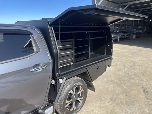 A truck with a canopy and shelves in the back is parked in a parking lot.