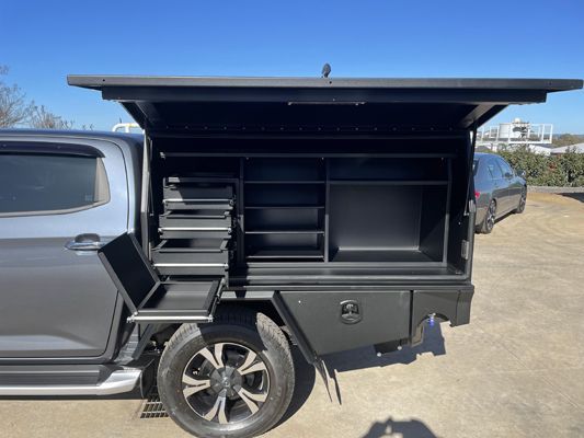 A black truck with a canopy and drawers is parked in a parking lot.