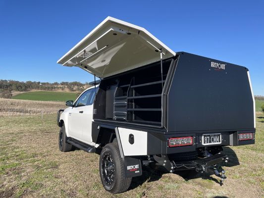 A white truck with a black canopy is parked in a field.