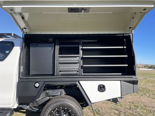 The back of a white truck with the canopy open and shelves.