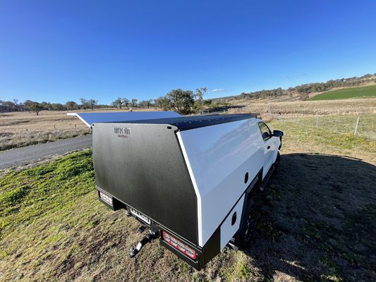 A white truck with a black canopy is parked in a field.