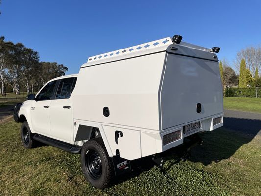 A white truck with a canopy on top of it is parked in the grass.