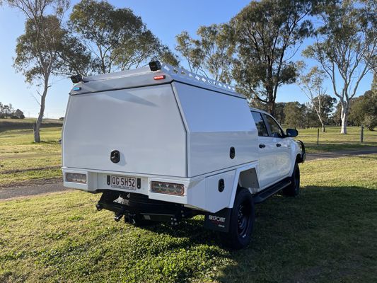 A white truck with a canopy is parked in a grassy field.