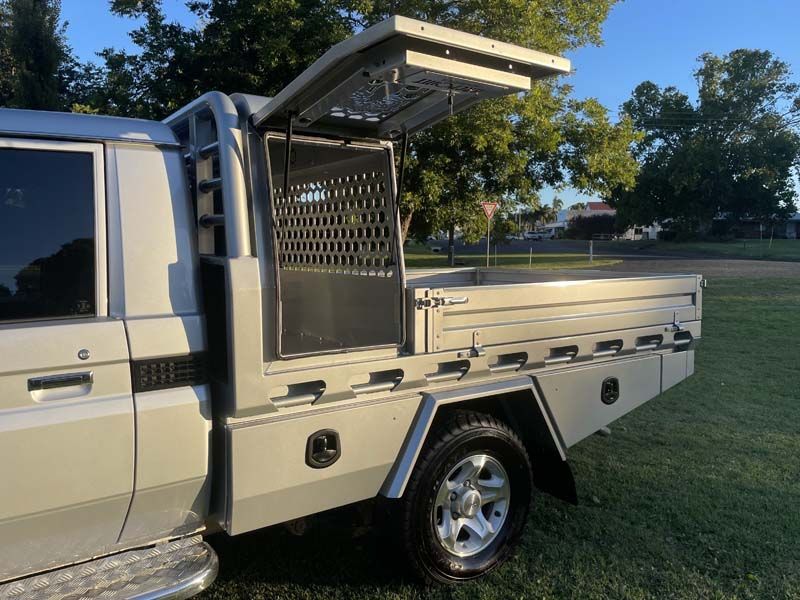 A silver truck with the bed open is parked in a grassy field.