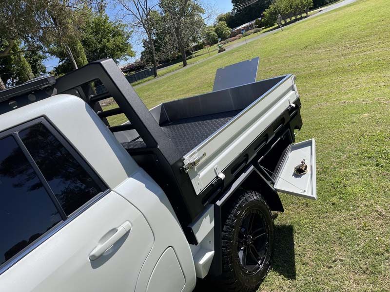 A white truck with a tray on the back is parked in a grassy field.