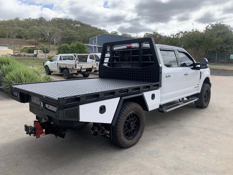 A white truck with a flat bed is parked on the side of the road.