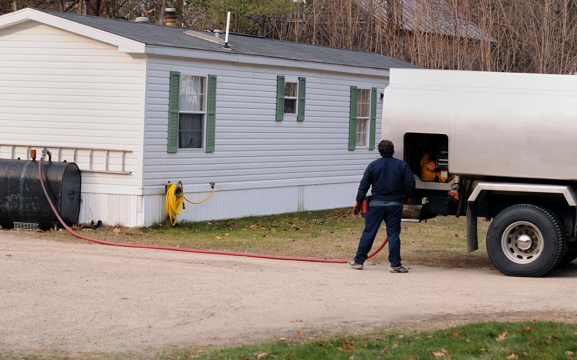 A man is standing next to a tanker truck in front of a mobile home.