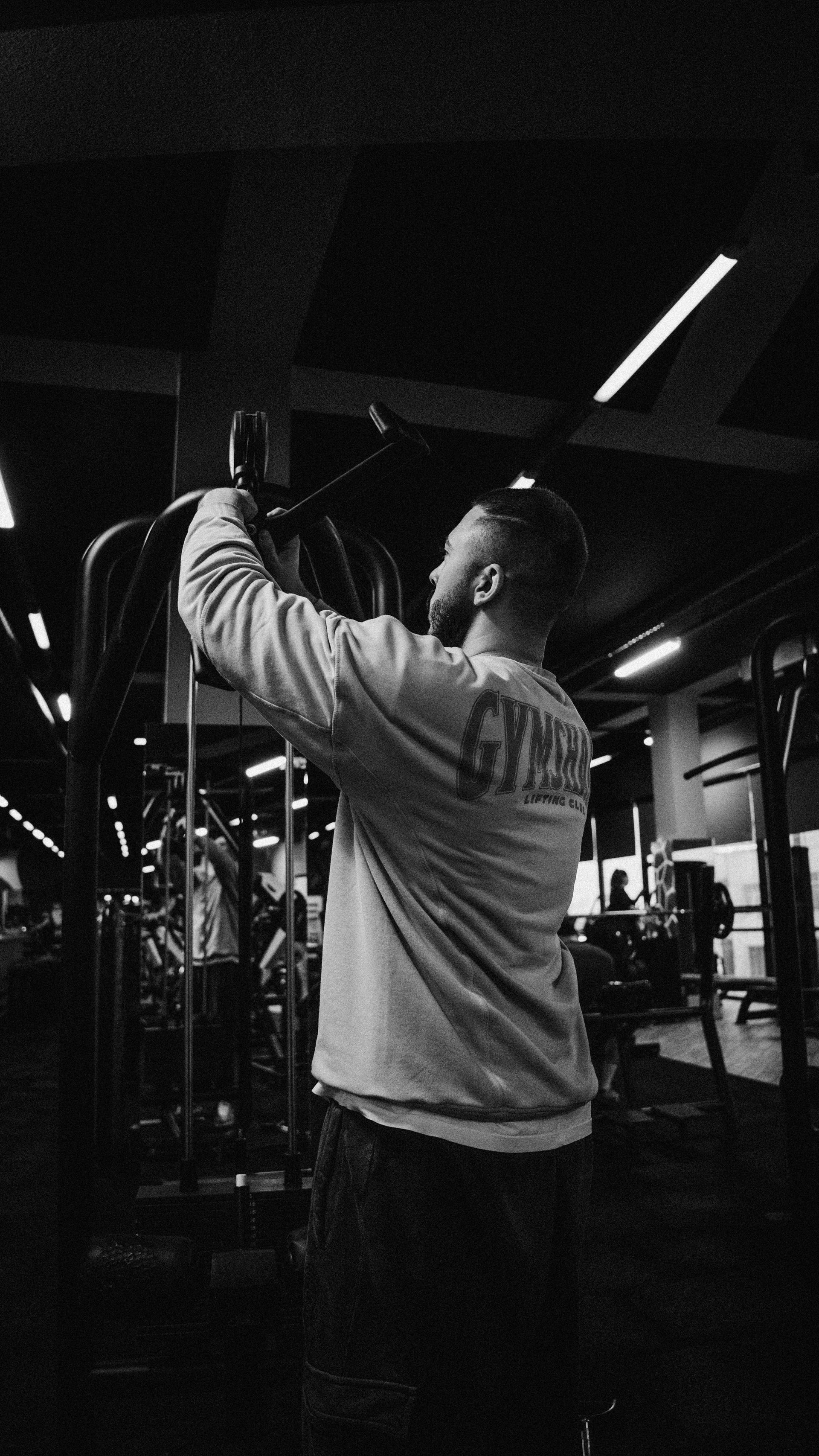 Een persoon stelt een fitnessapparaat af in een donkere, zwart-witte fitnessruimte.