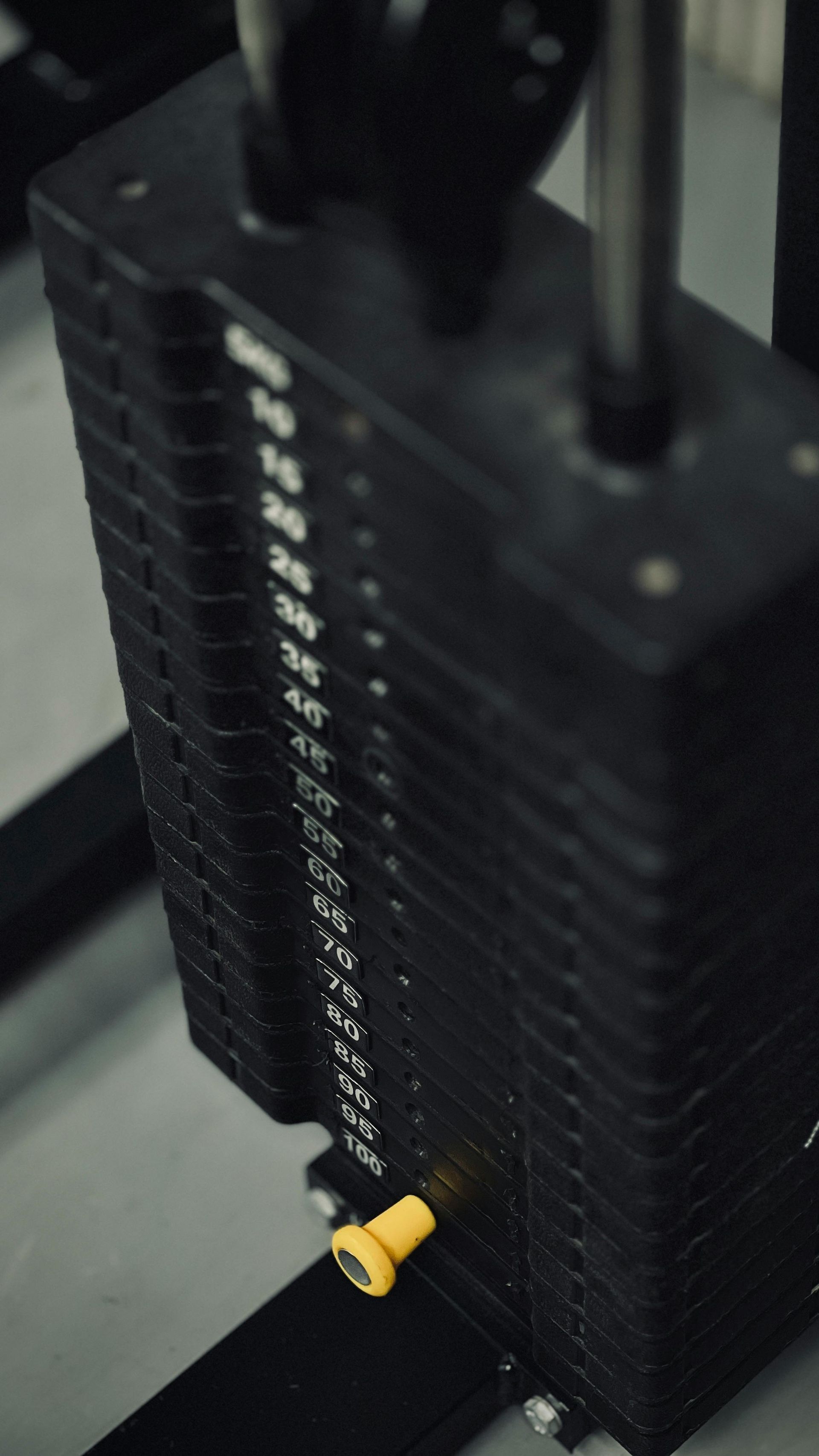 Zwarte gewichtenstack voor de sportschool met een gele selectiepin en metalen geleidestangen.