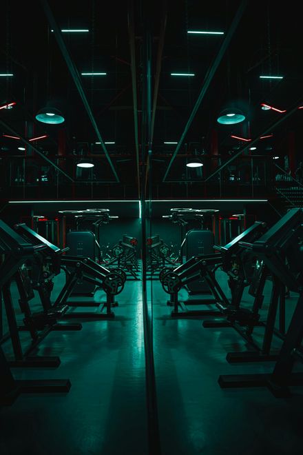 Een schemerige, neonverlichte sportschool met loopbanden, gloeiende turquoise en rode lampen en spiegelwanden.