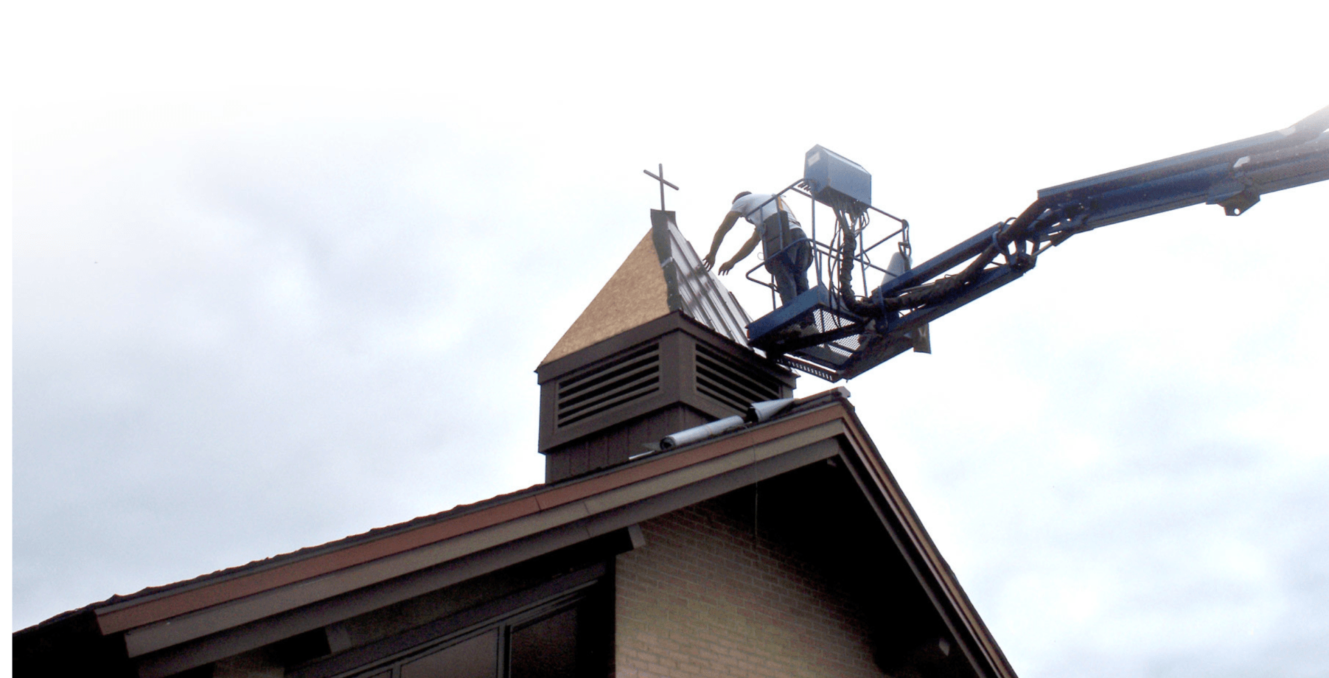 crane lifting worker to renovate hip style roof of a church