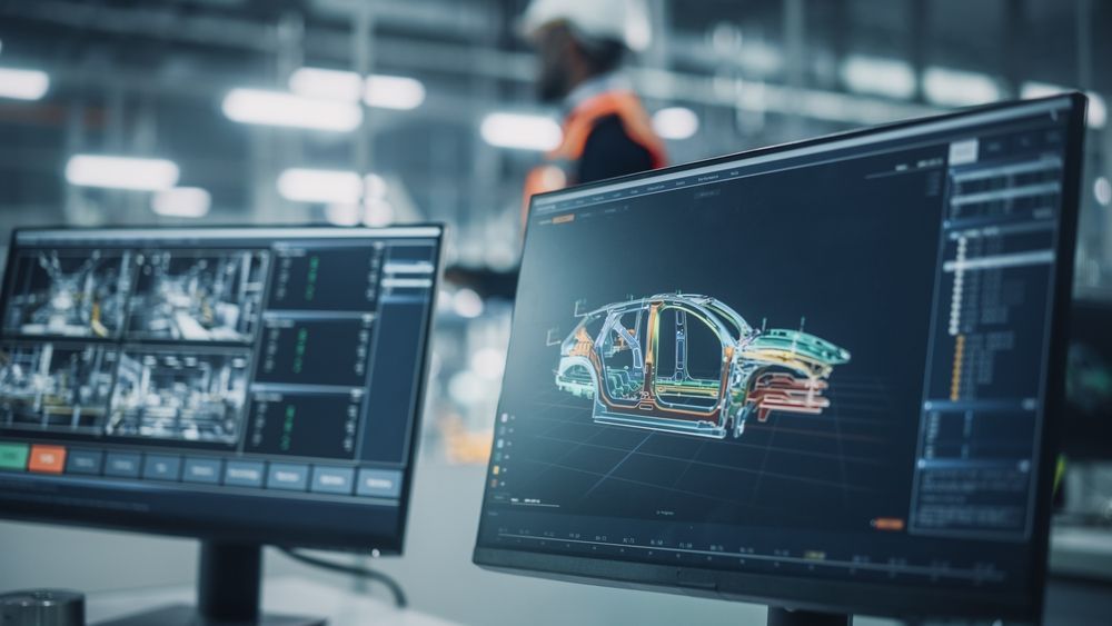 A computer monitor with a picture of a car on it in a factory.