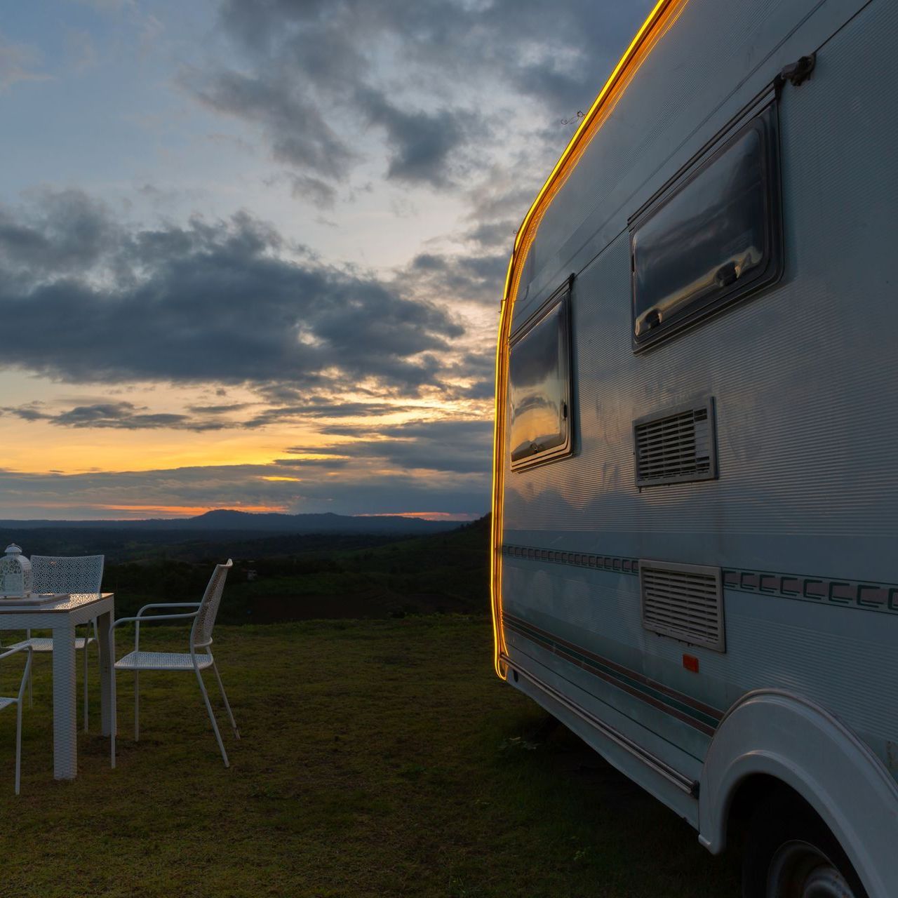 A camper is parked in the grass with a table and chairs in front of it