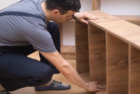 A man is kneeling down and touching a wooden shelf.