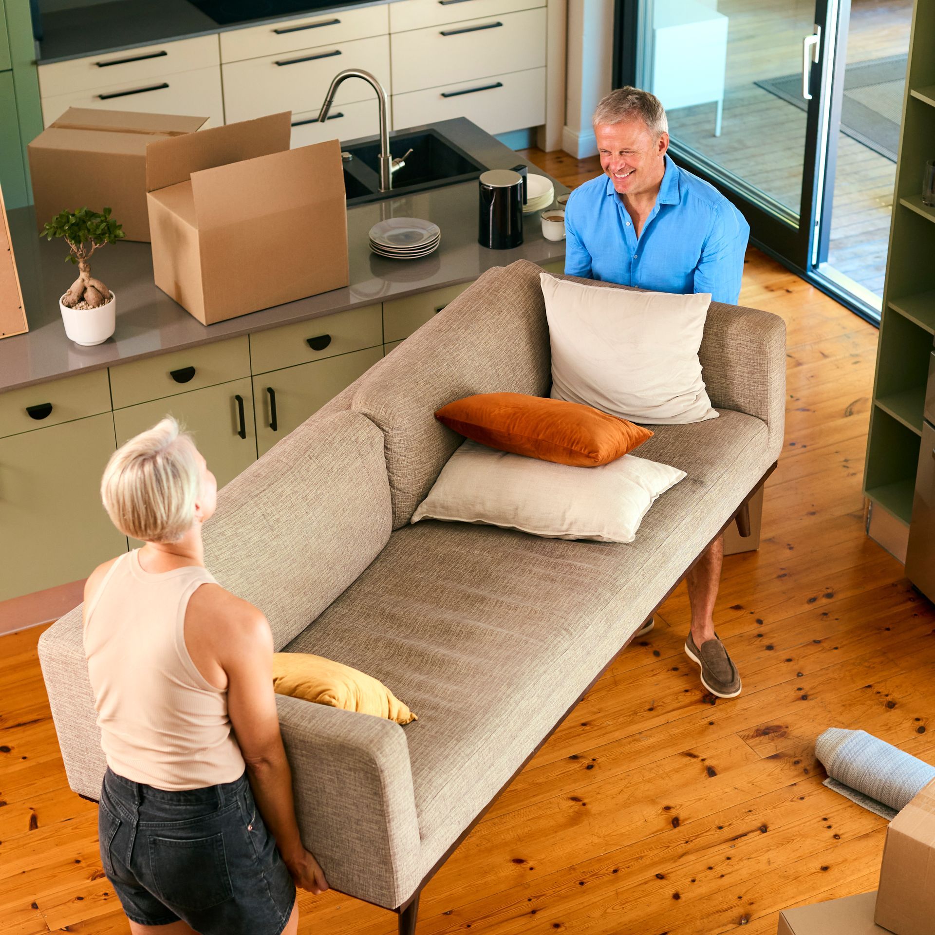 A man and a woman are moving a couch in a living room