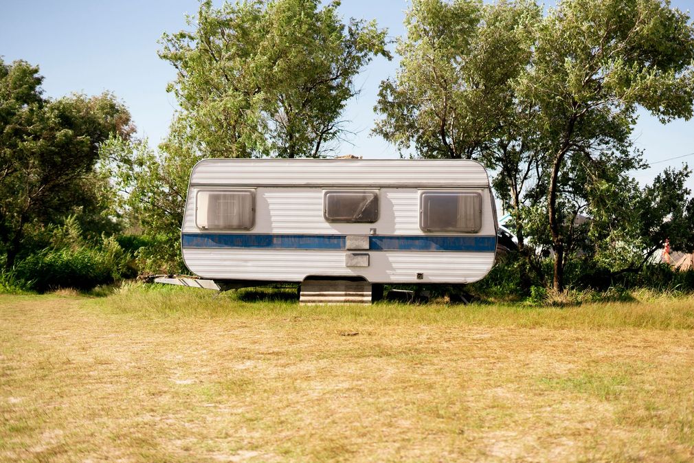 A white and blue trailer is parked in a grassy field.