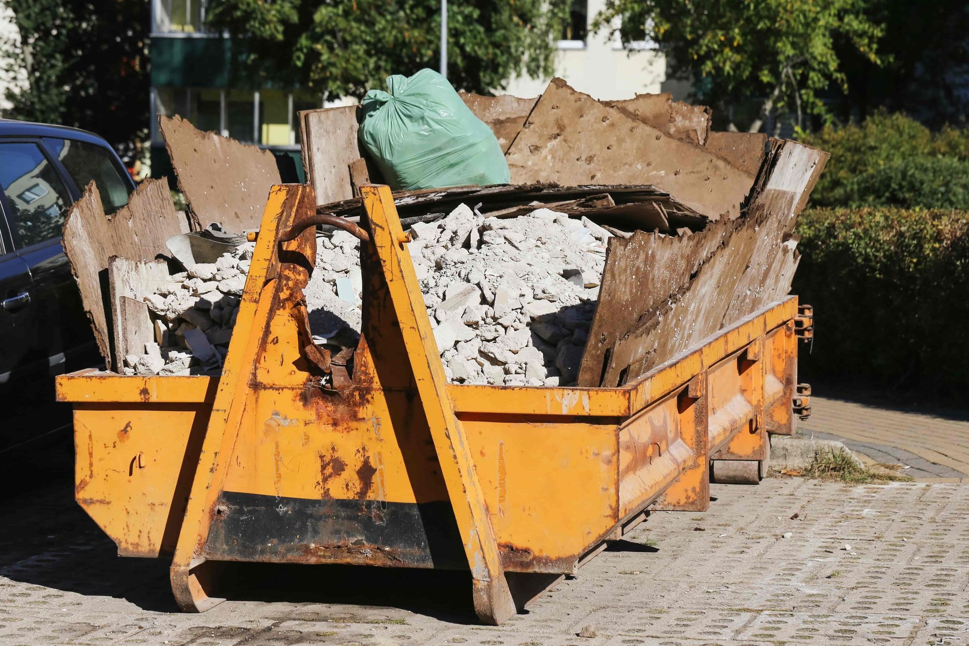 Orange construction dumpster filled with rubble and wood on a paved street