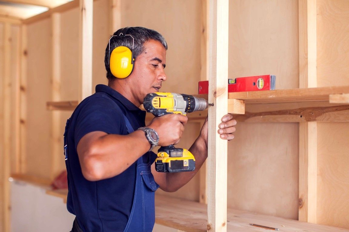 A man wearing a jumper is drilling in the wood.