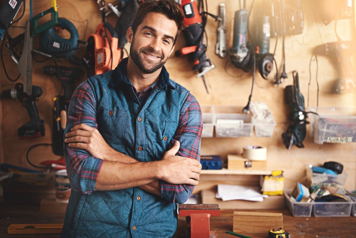 A man smiling with a variety of tools on the wall.
