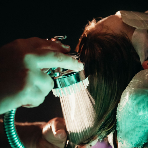 A hand holds a showerhead rinsing hair in a dimly lit, green-tinted setting.