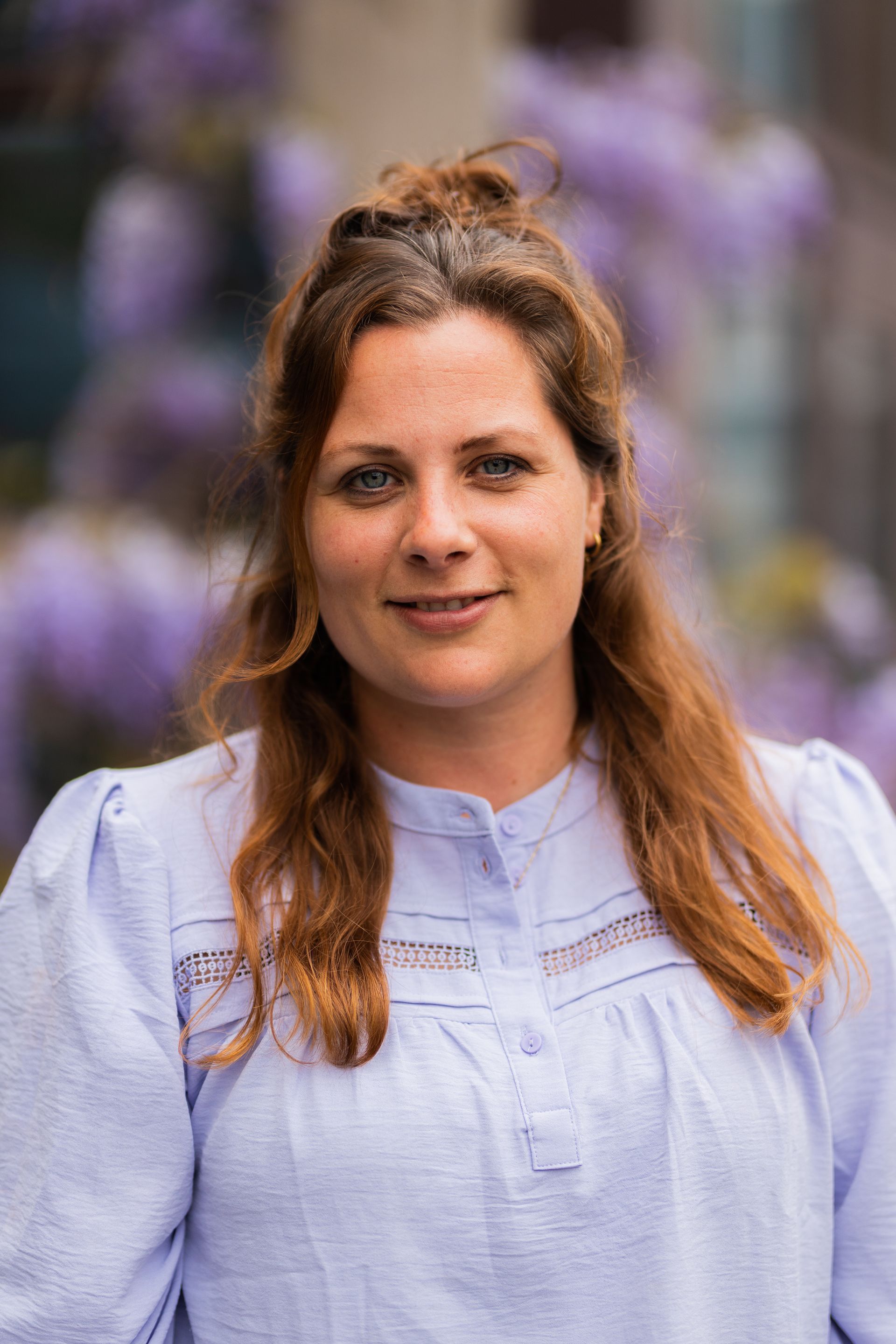 Een vrouw in een blauw shirt staat voor paarse bloemen.