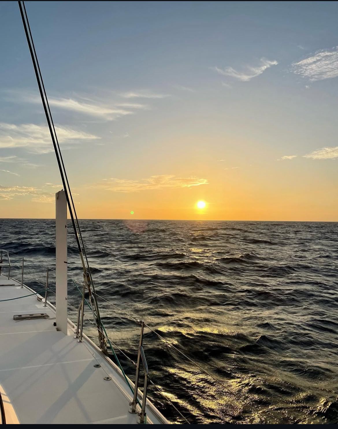 Een zeilboot drijft op een groot wateroppervlak bij zonsondergang.