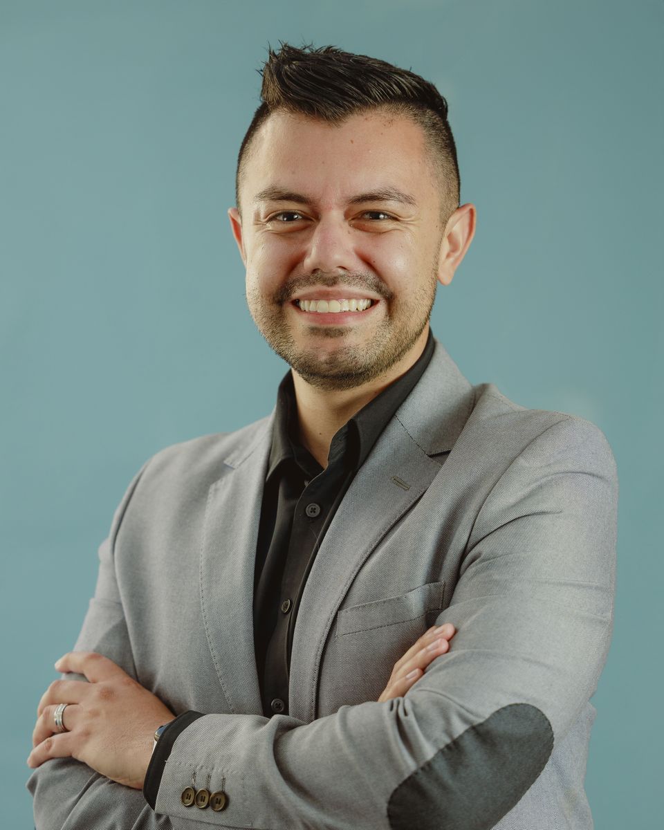 Man in gray blazer, arms crossed, smiling, against a blue backdrop.
