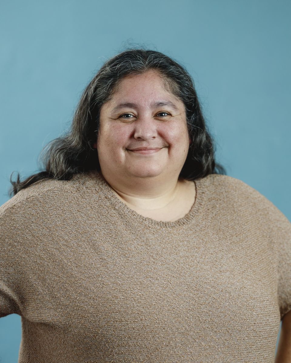 Woman in a brown sweater smiles at the camera against a blue background.