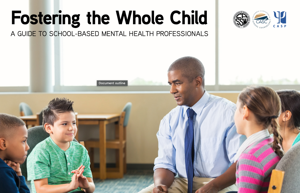 A man in a tie speaks to a group of children in a school setting.
