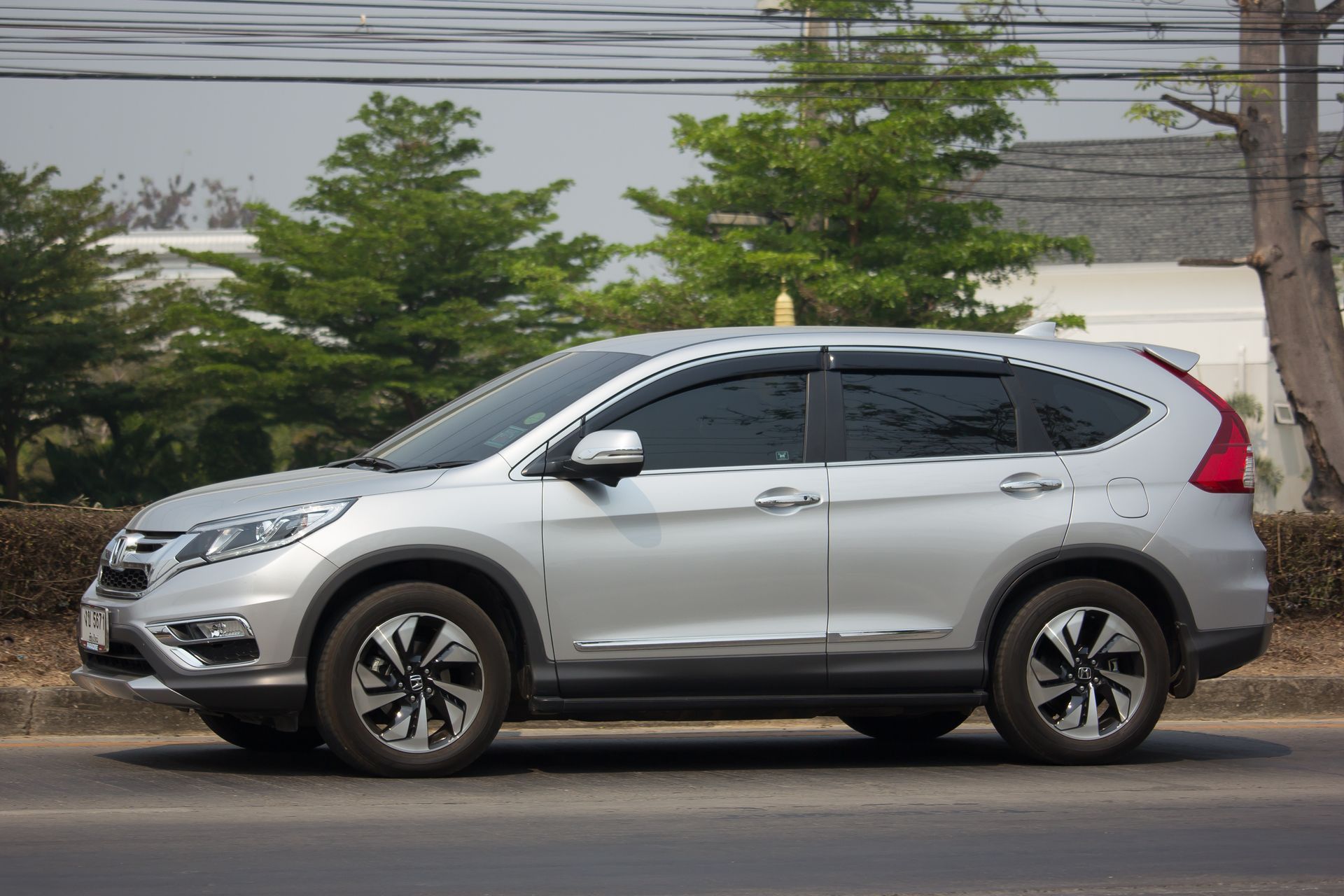 Silver Honda CRV SUV parked on a road, with trees and a building in the background.