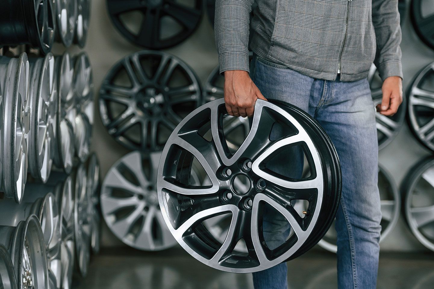 A man is holding a car wheel in front of a wall of wheels.