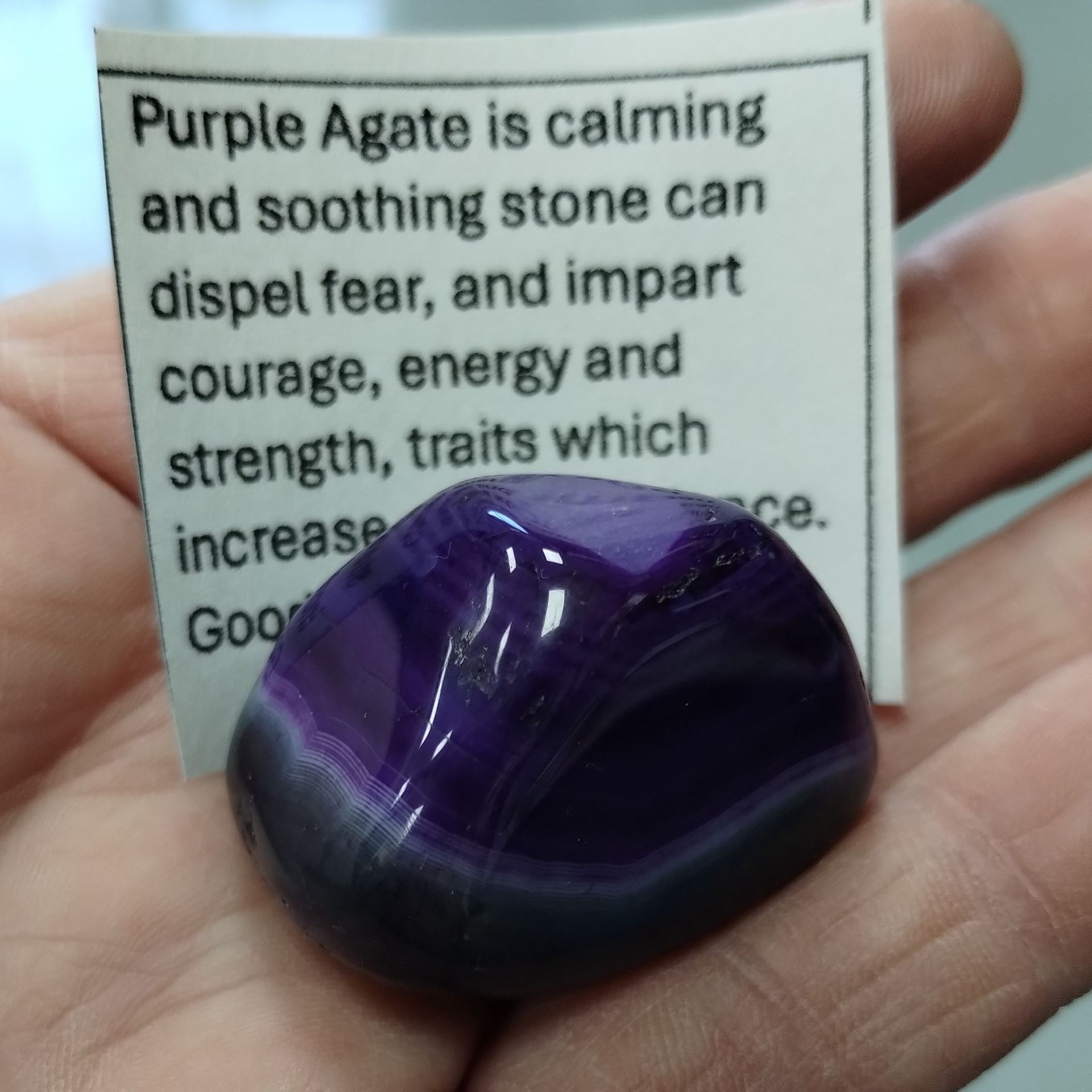 Hand holding a polished purple agate stone with a description card.