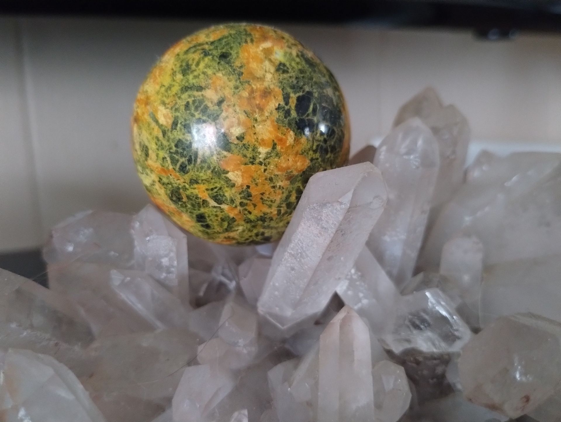 Yellow and green patterned sphere sits on a cluster of clear quartz crystals.