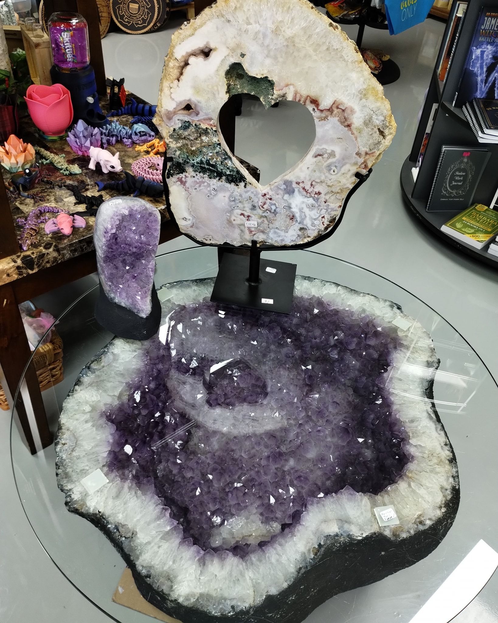 Amethyst geode table with heart-shaped opening, purple crystals, glass top, shop setting.