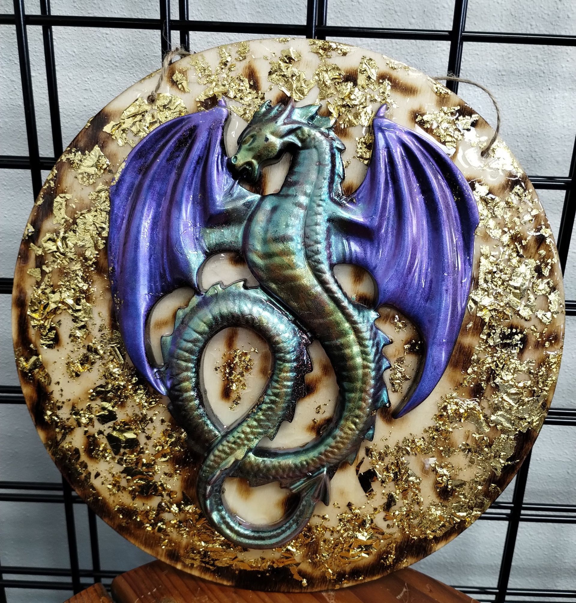 Circular artwork: dragon with purple wings, iridescent green body on gold-flecked, tan background.