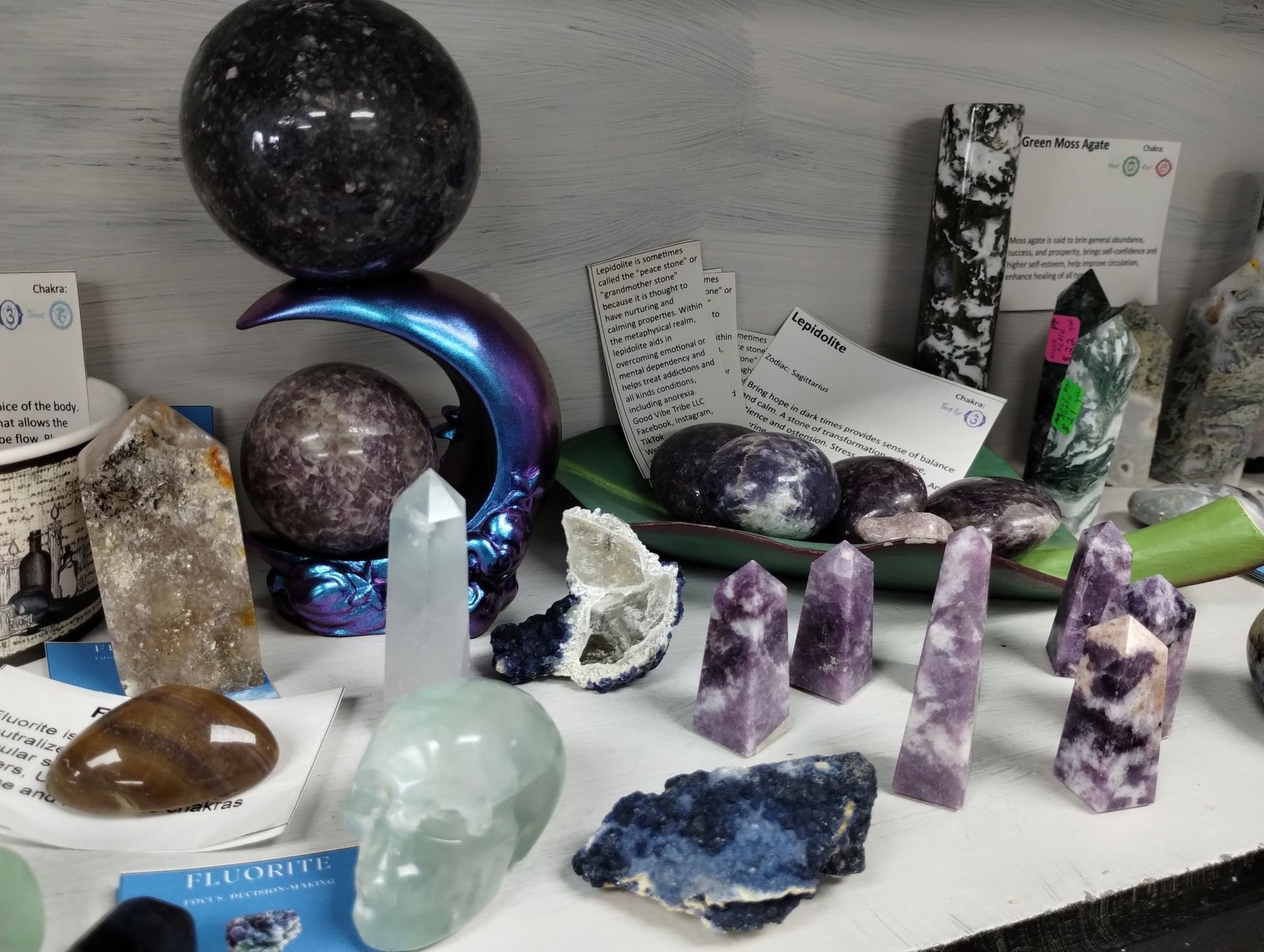 Shelf of crystals, including amethyst towers, a moon-shaped stand, and a fluorite skull, various colors.