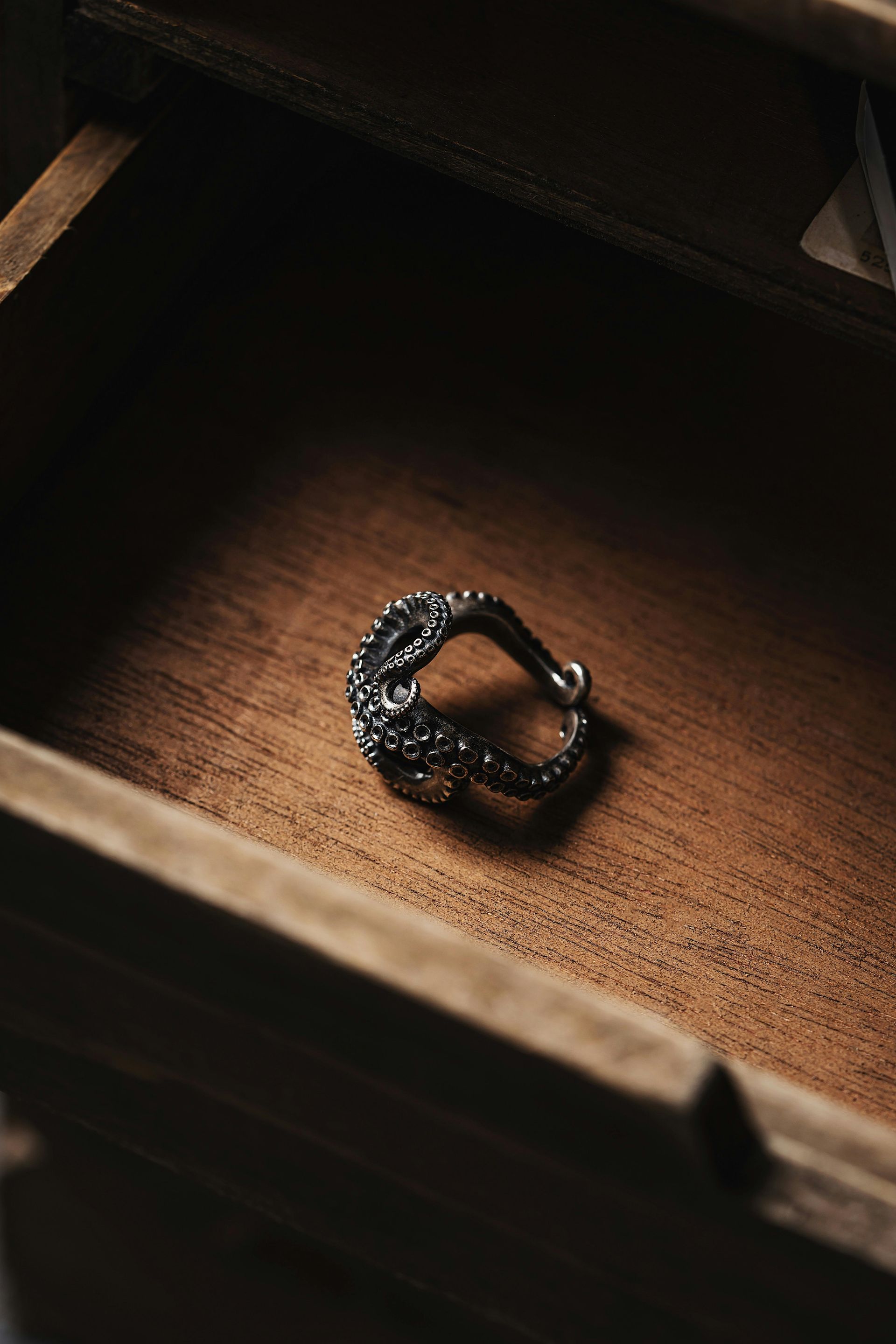 Silver ring with ornate details rests inside a wooden drawer.
