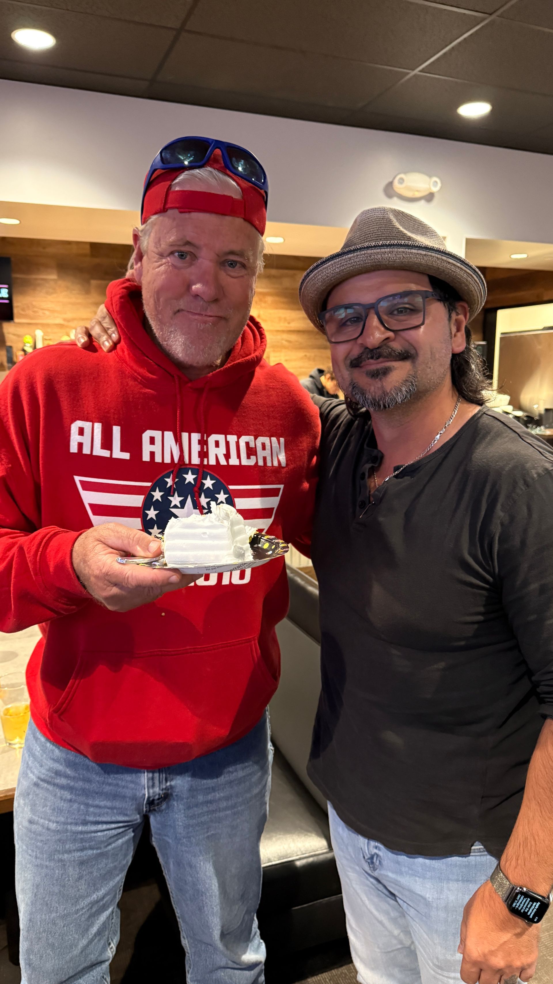 Two men are posing for a picture while one of them is holding a piece of cake.