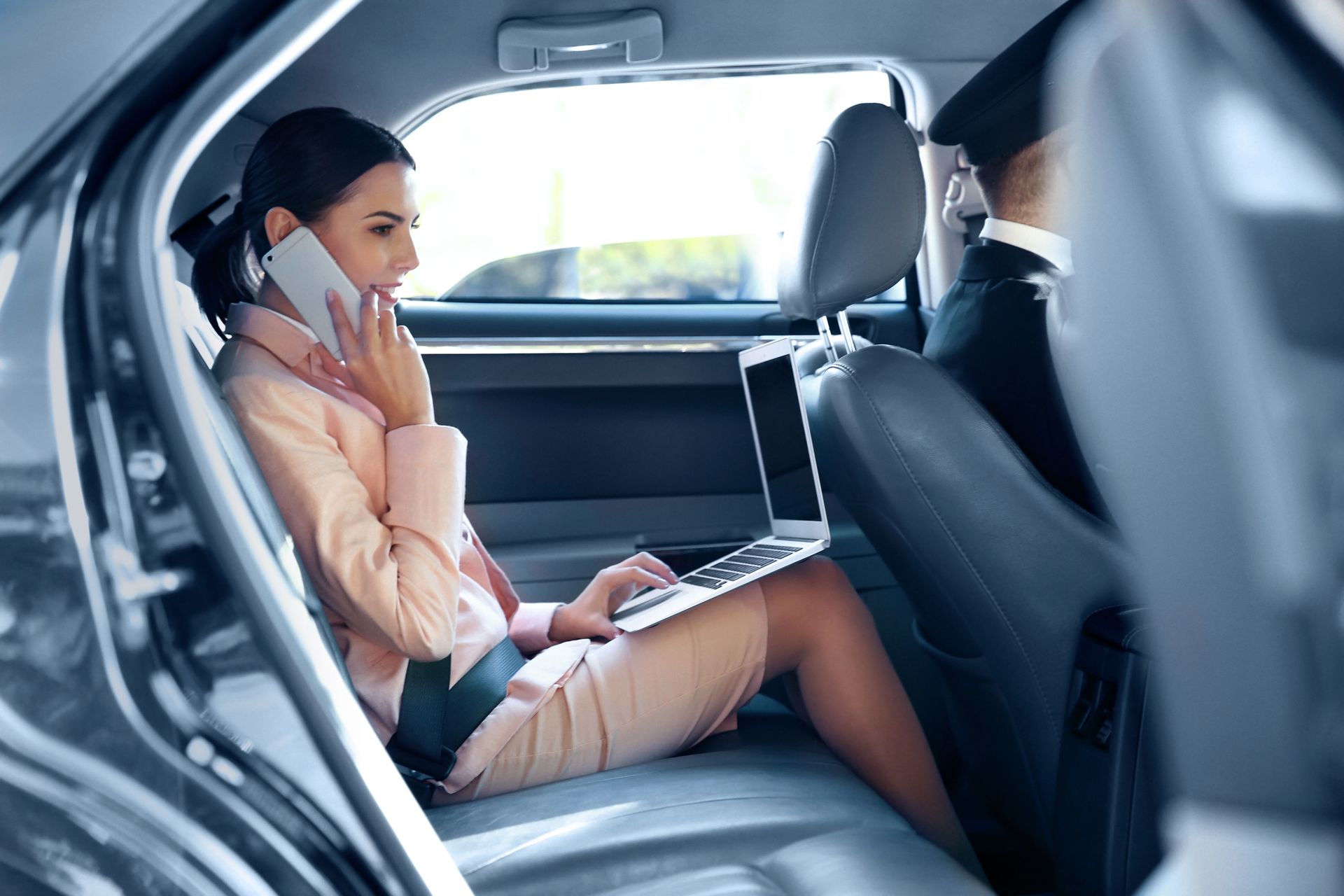a woman is sitting in the back seat of a car using a laptop and talking on a cell phone .