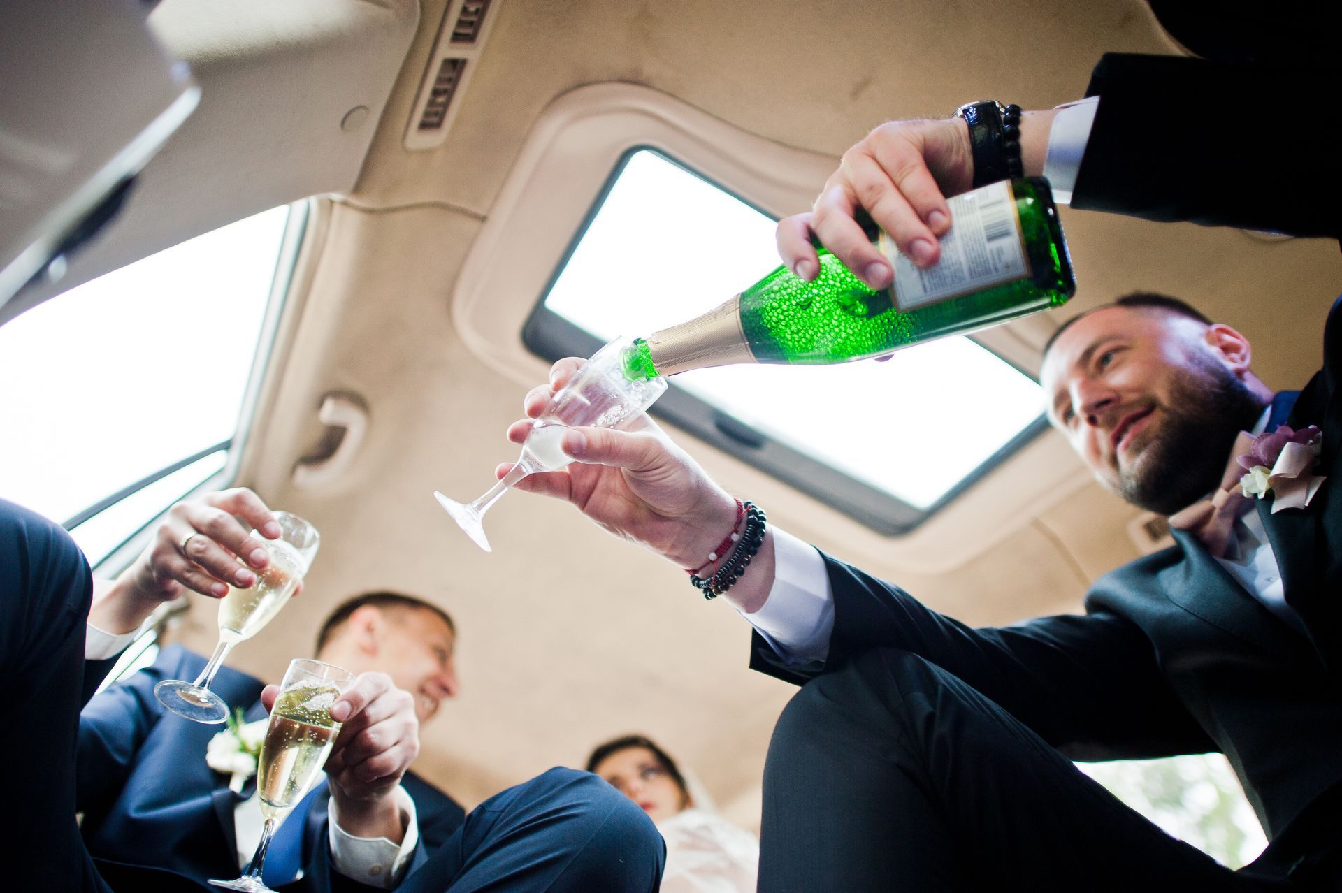 A man is pouring champagne into a glass in a car.