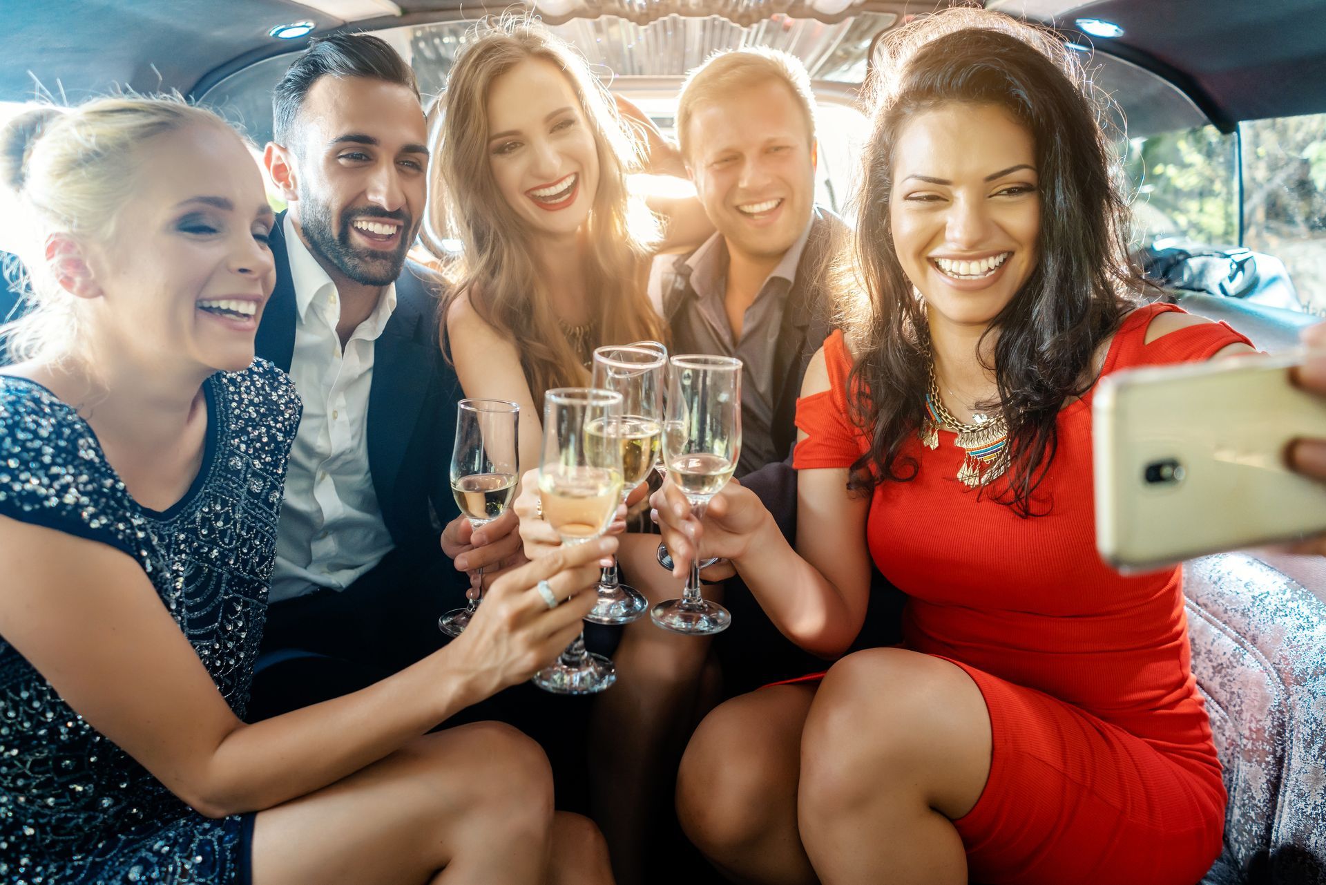 a group of people are sitting in a limousine drinking champagne and taking a selfie .