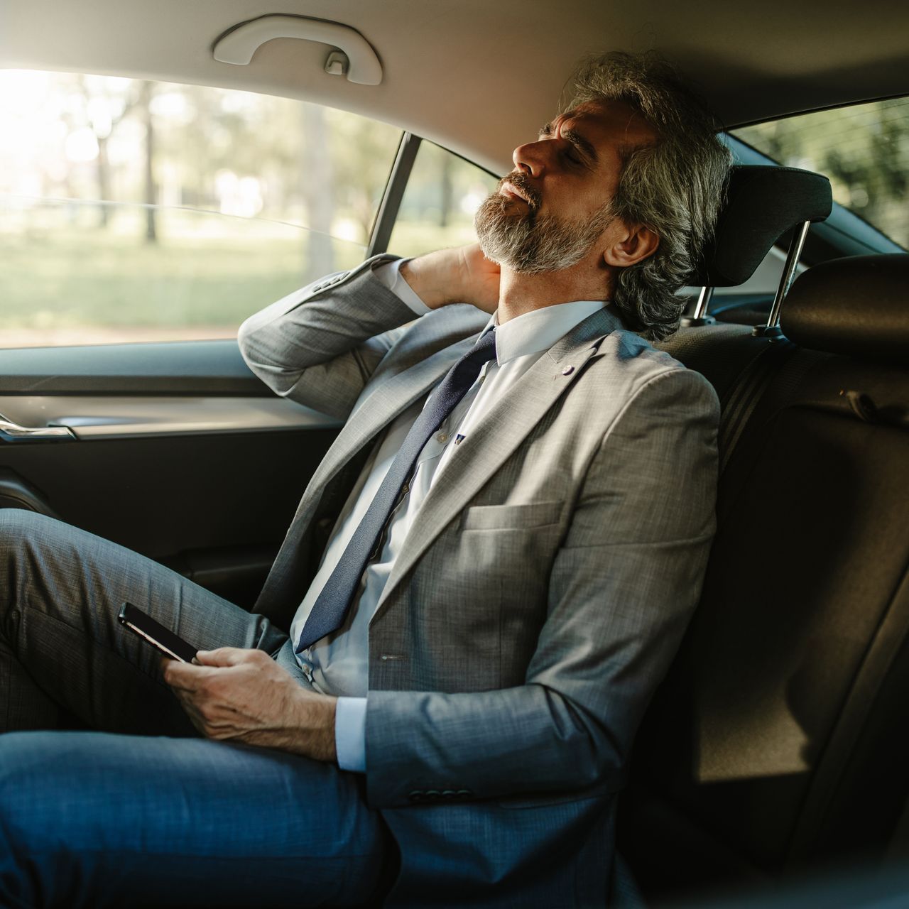 A man in a suit and tie is sitting in the back seat of a car