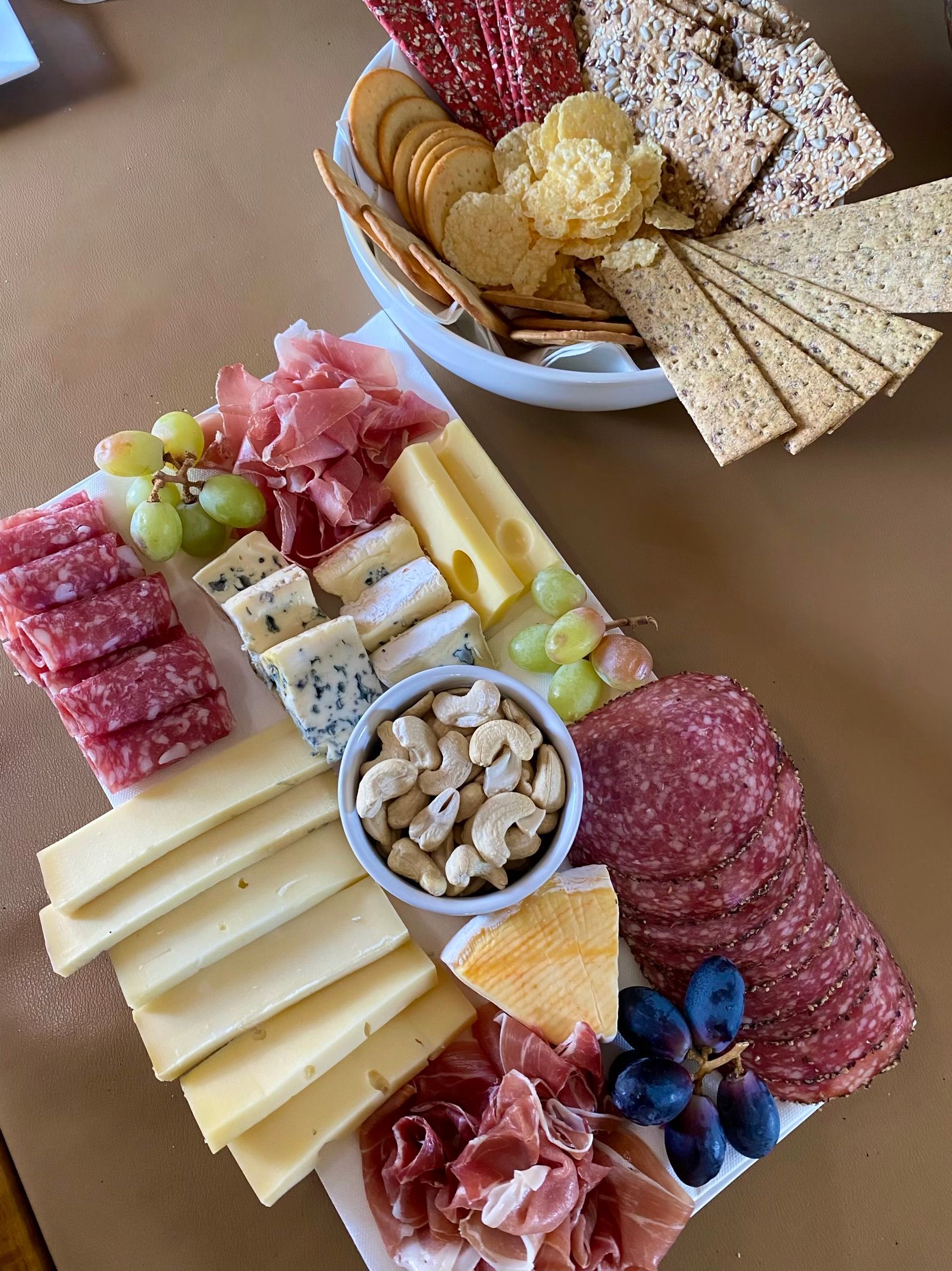 A tray of cheese , crackers , grapes and meat on a table.
