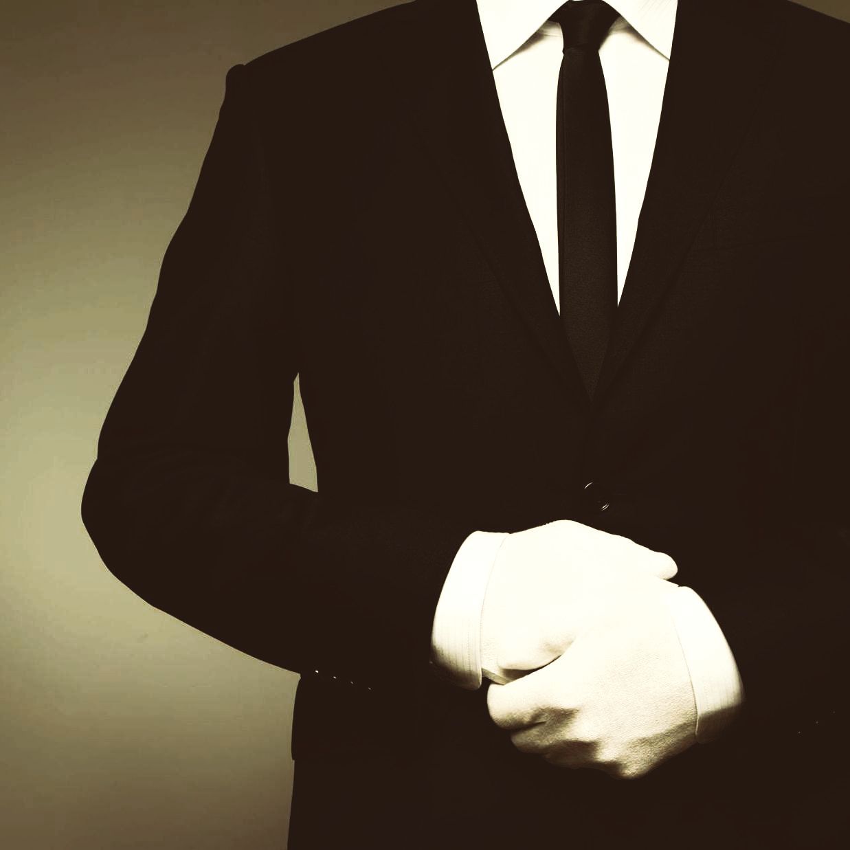A man in a suit and tie is wearing white gloves