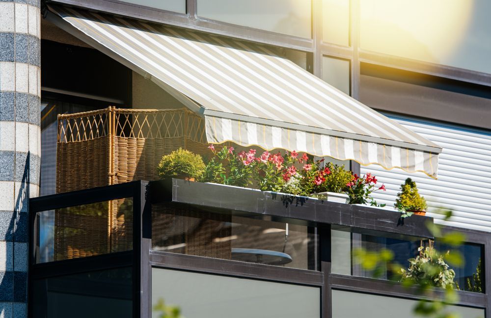 A Balcony With a Striped Awning and Flowers on It — Simply Smarter Blinds in Tea Gardens, NSW