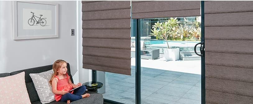 A Little Girl is Sitting on a Couch in Front of a Sliding Glass Door — Simply Smarter Blinds in Tea Gardens, NSW