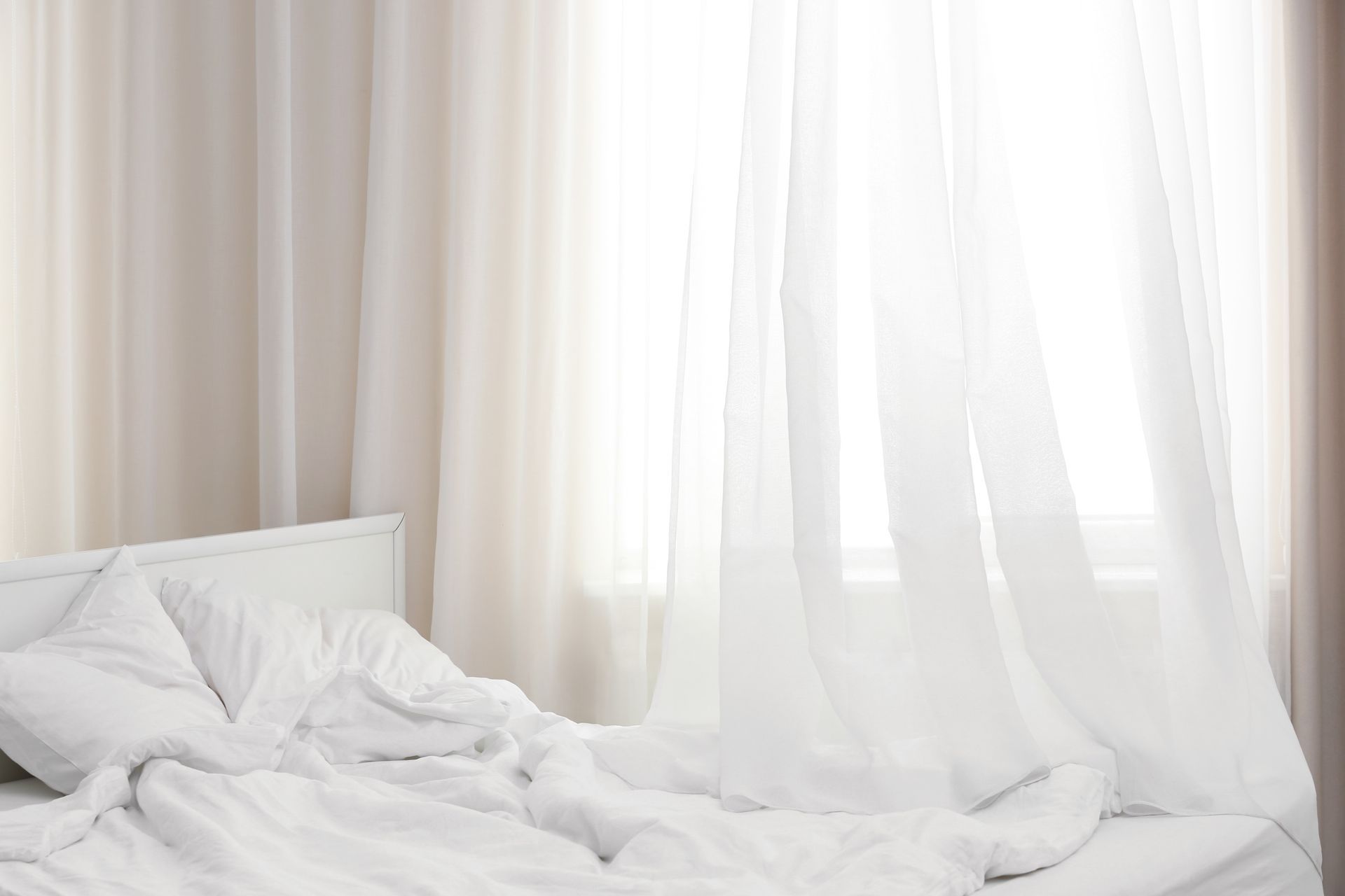 A Bed With White Sheets and Pillows in a Bedroom Next to a Window — Simply Smarter Blinds in Tea Gardens, NSW