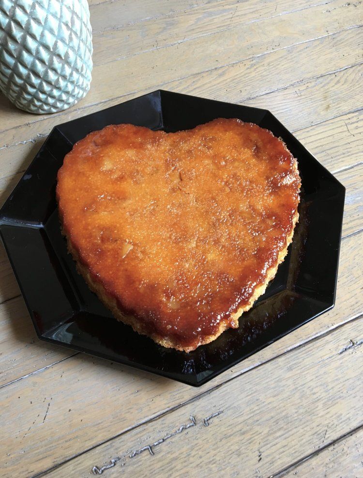 Un gâteau en forme de cœur sur une assiette noire sur une table en bois.