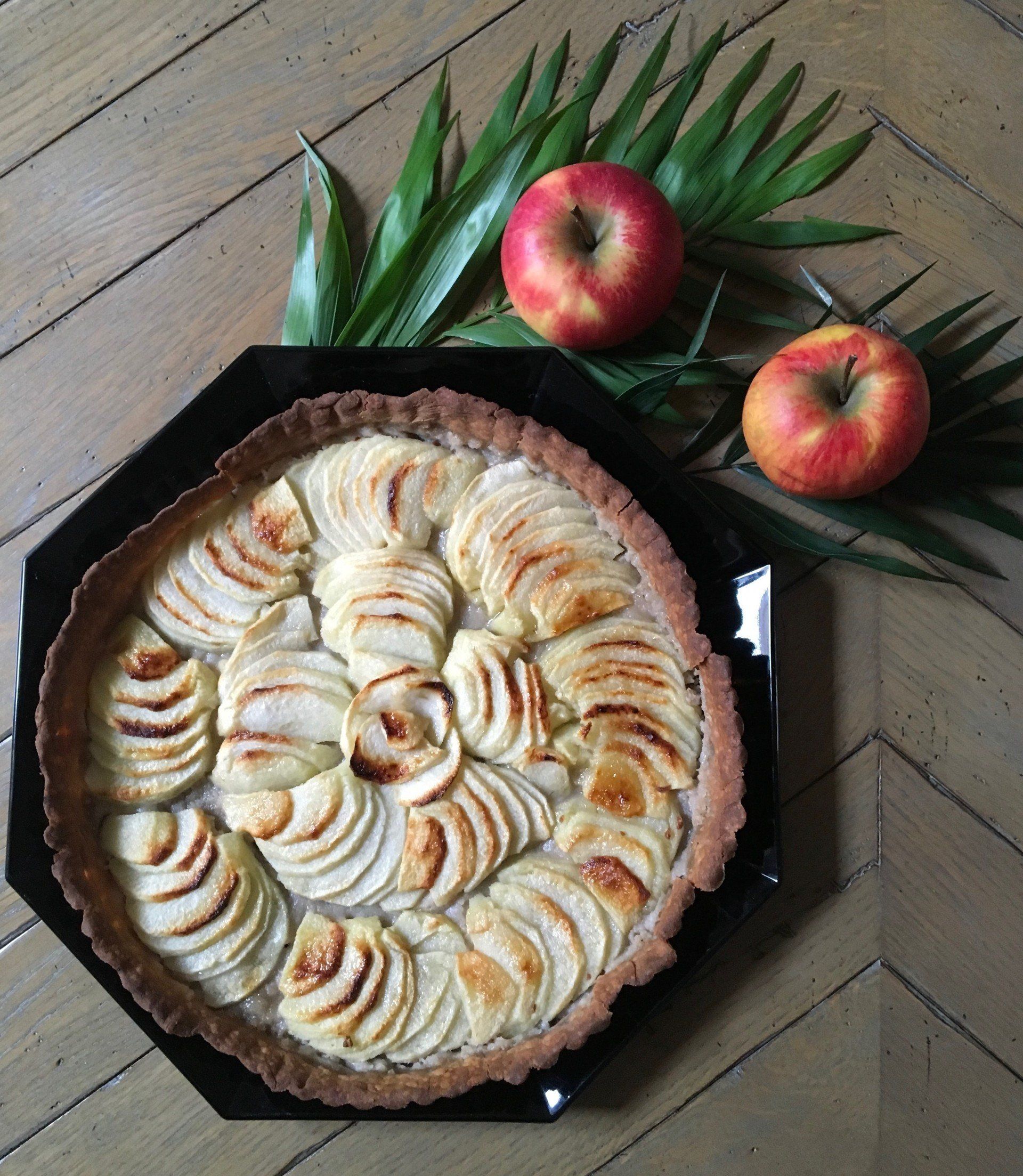 Une tarte aux pommes est posée sur une table en bois à côté de deux pommes