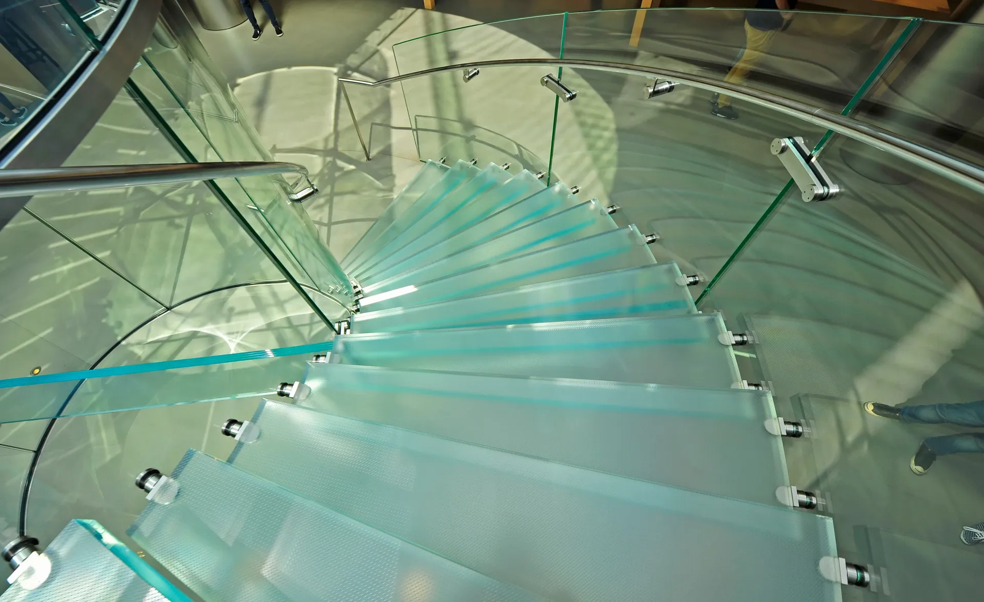 Glass spiral staircase, transparent steps, metal railing, indoors, overhead view.